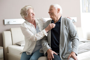 Altes Ehepaar ist pflegende Angehörige und Pflegebedürftiger und sitzen auf dem Pflegebett.