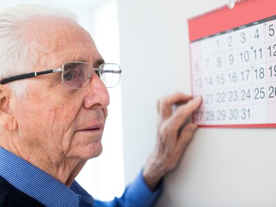 Verwirrter Mann mit Demenz schaut auf einen Wandkalender